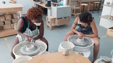 Two women sculpt pottery on turntables in a studio.