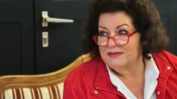 Frau mit roten Brille sitzt auf einem Sofa.