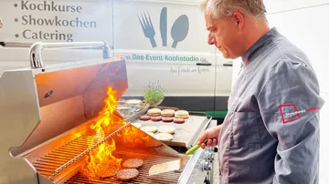 Ein Koch grillt Burger mit Flammen in einem Catering-Kontext.