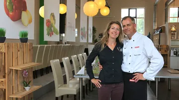 Paar steht lächelnd in einem modernen Restaurant mit Pflanzen.