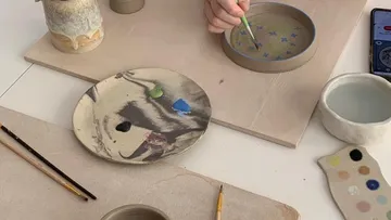 A hand paints with a brush on a ceramic bowl.
