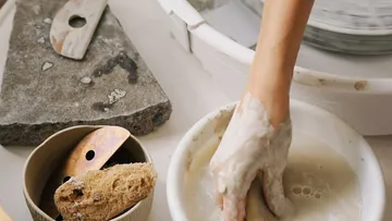 A hand works with clay in a bowl.
