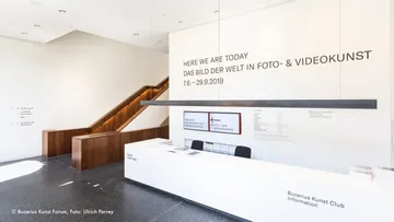 Empfangstheke mit Kunstinformationen in heller Galerie.
