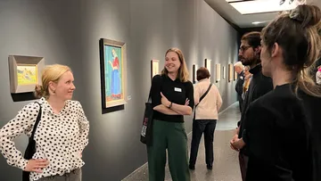 Personen betrachten Bilder in einer Galerie, unterhalten sich.