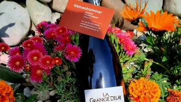 A bottle of wine stands between colorful flowers and stones.