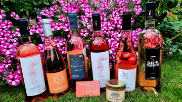 Six bottles of rosé wine stand in front of colorful flowers.