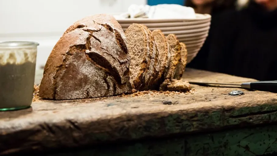 Brot auf einem Holztisch, in Scheiben geschnitten, umgeben von Menschen.
