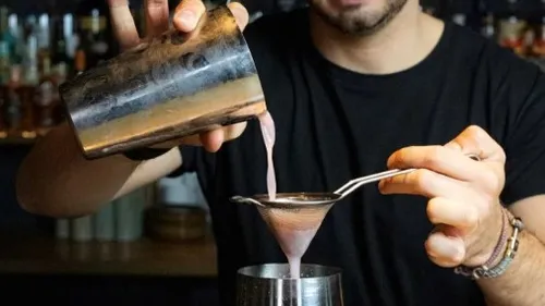 Bartender pours a cocktail through a sieve into a glass.