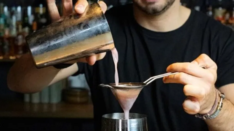 Barkeeper gießt einen Cocktail durch einen Sieb in ein Glas.