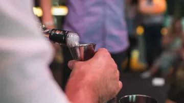 A hand pours vodka into a measuring cup, convivial setting.