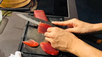 Ein Koch schneidet frischen Thunfisch auf einem Brett.