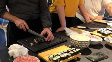 Person, die Sushi auf einem schwarzen Tablett schneidet.