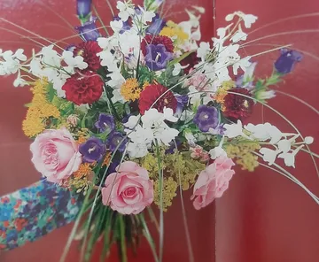 Blumenstrauß in bunten Farben, gehalten vor rotem Hintergrund.