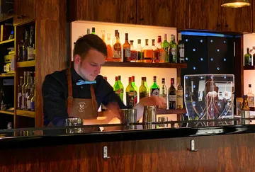 Bartenders mix drinks with spirits behind a bar.