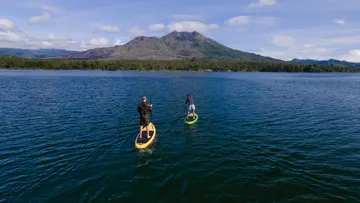 Zwei Paddelboarder auf einem See mit Bergkulisse.