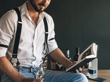 Man is reading a book while holding a glass of wine.