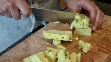 Käse wird in kleine Würfel geschnitten auf einem Holzbrett.