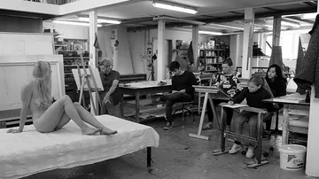 A nude model sits while artists draw in a studio.