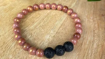 Ein Armband aus roséfarbenen und schwarzen Perlen liegt auf Holz.