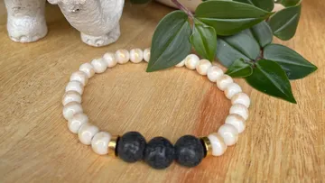 Armband liegt auf Holzoberfläche mit Pflanzen im Hintergrund.