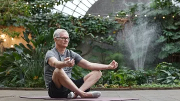 Man meditating in a garden with plants and waterfall.