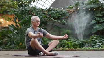 Man meditates on a mat in a garden.