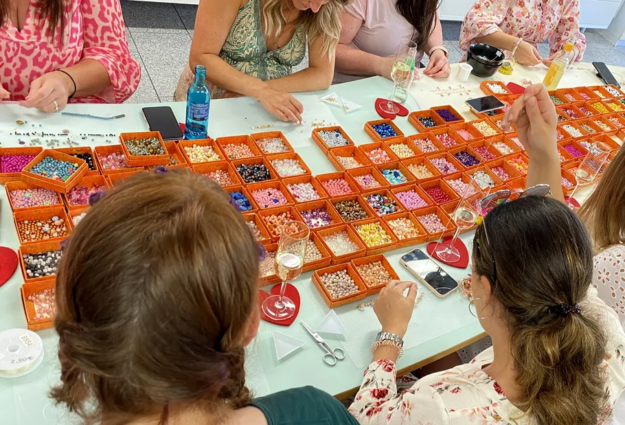 FarbenTeam feiert mit einem Armband Design Workshopfrohe Perlen auf einem Tisch, Frauen beim Basteln.