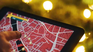 Tablet, auf dem die Karte mit dem Finger gezeigt wird, festliche Lichter.