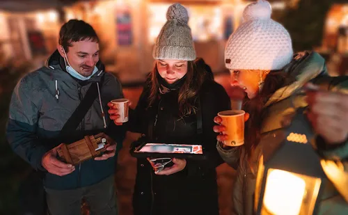 Three people look at a tablet together at night.