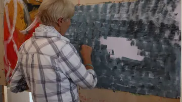 Eine Frau malt an einer großen Leinwand farbige Strukturen.