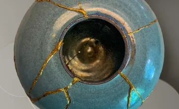 Türkise Vase mit Rissen und goldenen Füllungen, steht still.