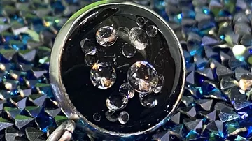 Schmuckstück reflektiert Licht, umgeben von glitzerndem Hintergrund.