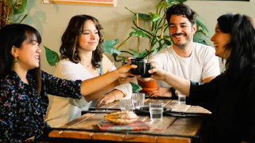 Friends toast with cups surrounded by plants.