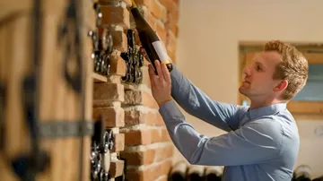 Man lifts a wine bottle in a wine cellar.
