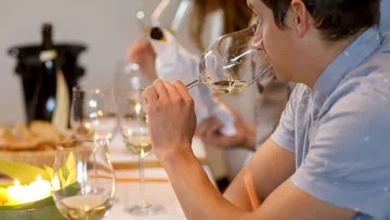 Man drinks wine at a table surrounded by friends.