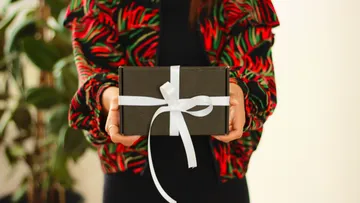 A person is holding a grey-wrapped gift with a ribbon.
