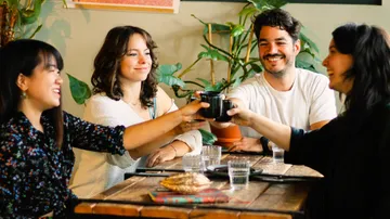 Four people toast with cups in a café.