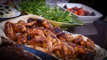 Gegrillte Hähnchenflügel liegen auf Fladenbrot neben Salat.