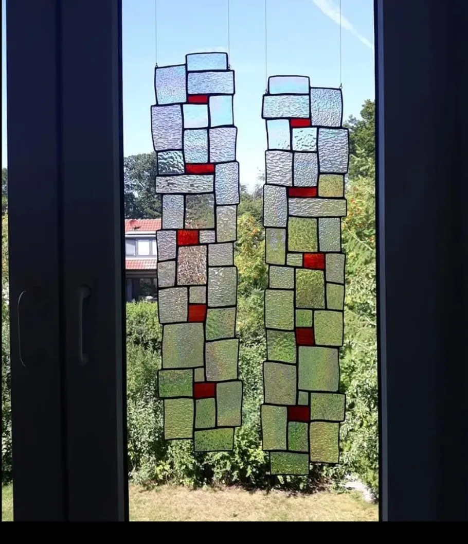 Buntes Glasdesign hängt am Fenster, Blick auf Garten.