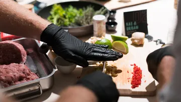 Hands cut ingredients on a table in a kitchen.