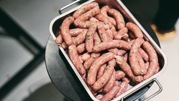 A metal pan with raw sausages on a table.