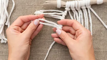 Hands tie knots with white threads on a table.