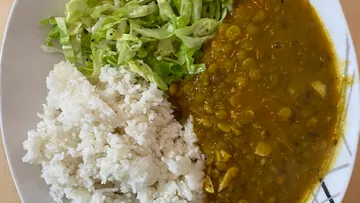 Reis, Linsen-Curry und Salat auf einem weißen Teller.