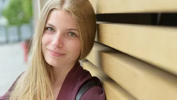 Young woman smiling, leaning against wooden background, urban context.