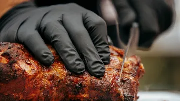 Ein Hand greift Fleischstück, während es geschnitten wird.