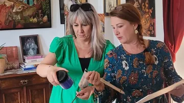 Two women look at painting colors in a room full of works of art.