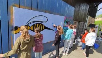 Jugendliche malen gemeinsam ein Bienenmotiv auf eine Wand.