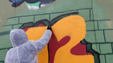 Artist sprays colorful graffiti on a wall.