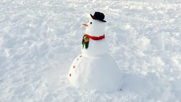 A snowman is standing in the snow, wearing a hat and scarf.