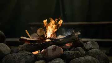 Fire burns on piles of wood surrounded by pebbles.